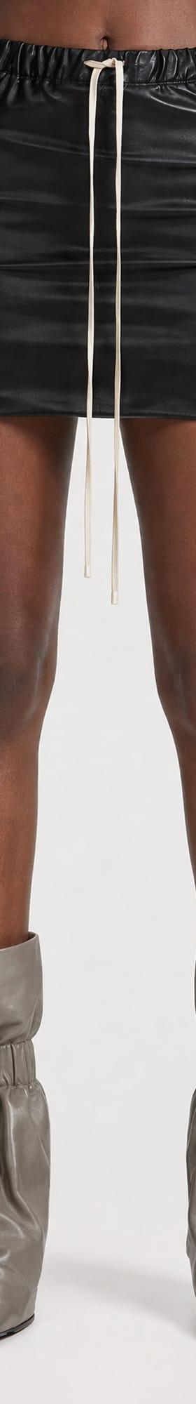 A woman wearing a black leather drawstring mini skirt with grey slouched leather boots