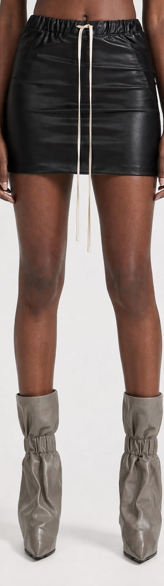 A woman wearing a black leather drawstring mini skirt with grey slouched leather boots