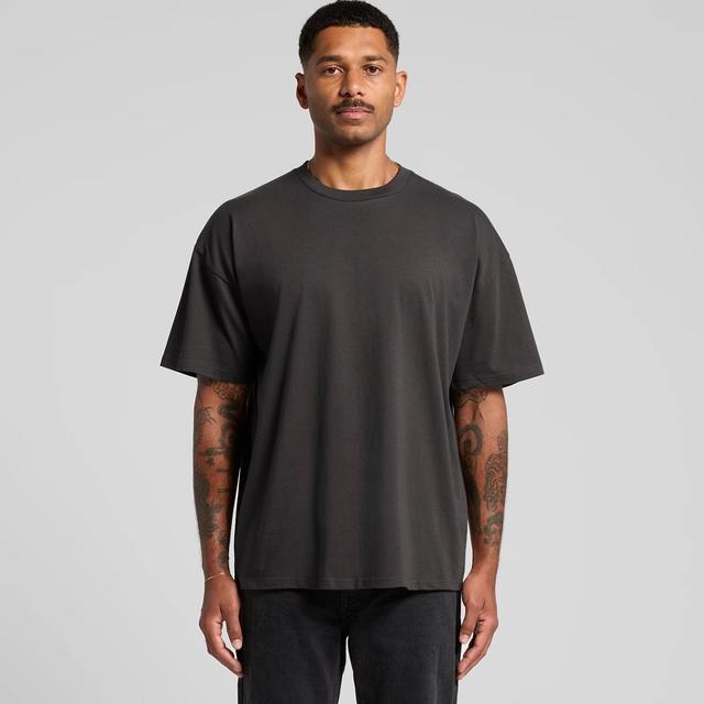 A man wearing a plain black AS Colour heavyweight crew-neck T-shirt with dropped shoulders and black jeans, on a pale grey studio background.