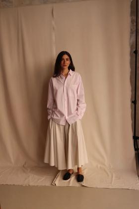 A woman wearing an oversized pale pink ATON cotton shirt with a white full skirt