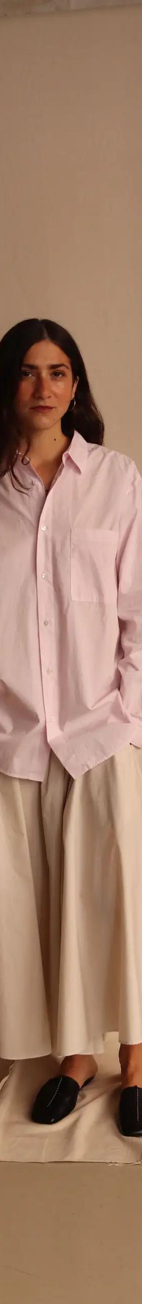 A woman wearing an oversized pale pink ATON cotton shirt with a white full skirt