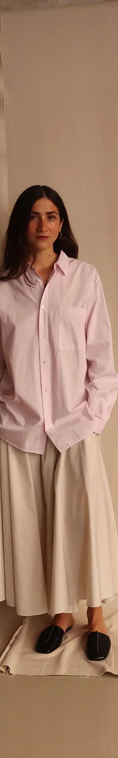 A woman wearing an oversized pale pink ATON cotton shirt with a white full skirt