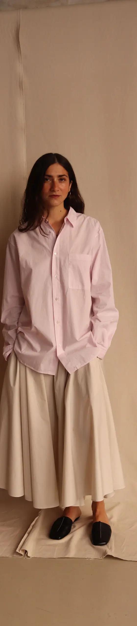 A woman wearing an oversized pale pink ATON cotton shirt with a white full skirt