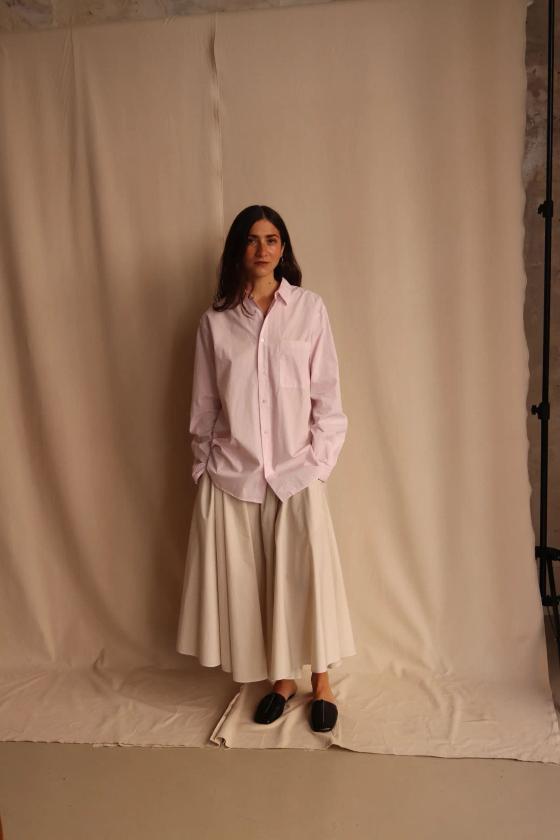 A woman wearing an oversized pale pink ATON cotton shirt with a white full skirt