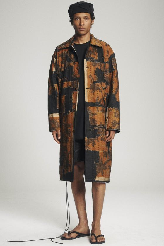 A man wearing a patchwork antique-textile Aubero coat with black shorts and sandals