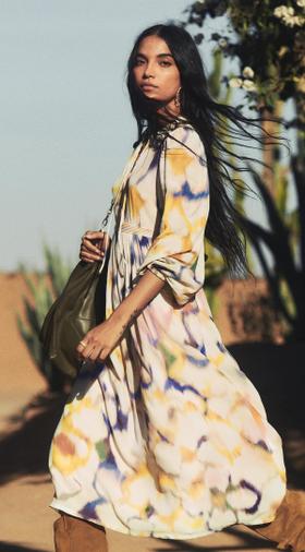 A woman wearing a floral-print ba&sh maxi dress with a green suede shoulder bag