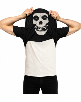 A man wearing a black and white Babylon LA x Misfits Fiend skull t-shirt pulled over his head