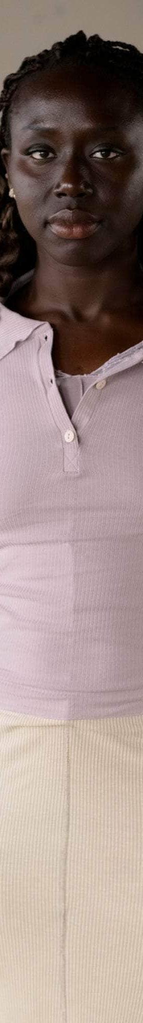 A woman wearing a lilac ribbed Baserange polo top with a cream knit skirt
