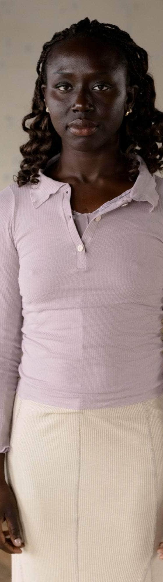 A woman wearing a lilac ribbed Baserange polo top with a cream knit skirt