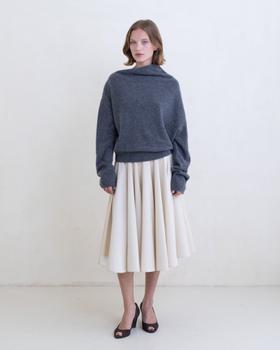 A woman wearing a grey Belle Anna funnel-neck sweater with a cream pleated midi skirt