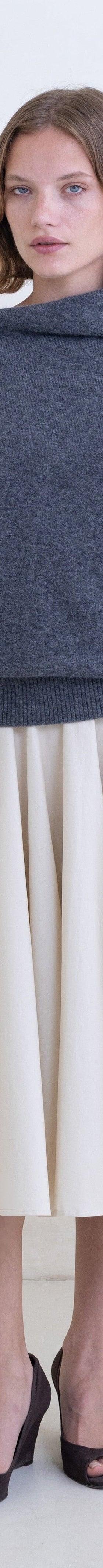 A woman wearing a grey Belle Anna funnel-neck sweater with a cream pleated midi skirt
