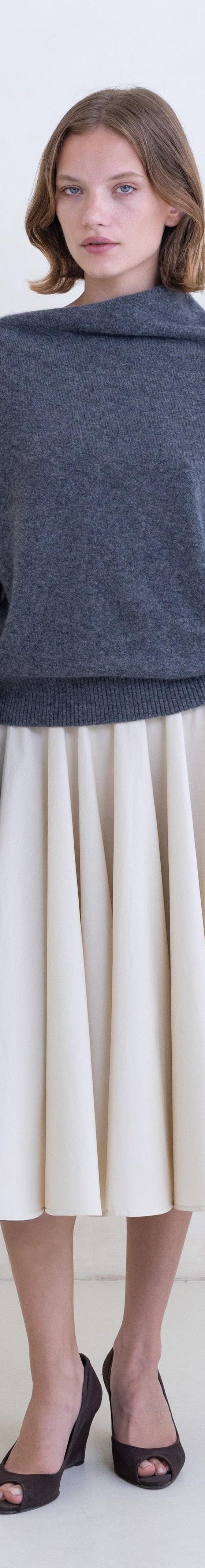 A woman wearing a grey Belle Anna funnel-neck sweater with a cream pleated midi skirt
