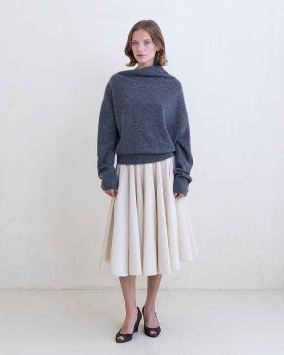 A woman wearing a grey Belle Anna funnel-neck sweater with a cream pleated midi skirt
