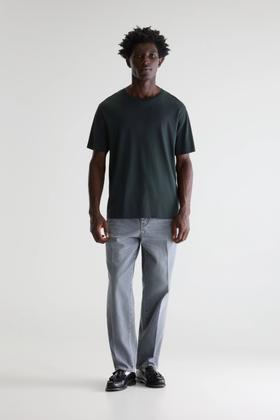 A man wearing a dark green Bellerose t-shirt and grey jeans
