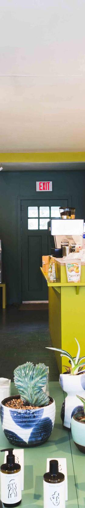 Interior of the Bellport General shop with shelves of provisions, a yellow coffee counter, and an aproned staff member