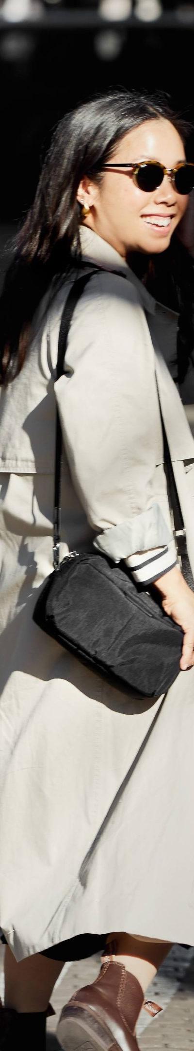 A woman wearing a beige trench coat with a black Bellroy crossbody bag