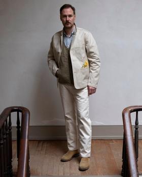 A man wearing a natural canvas Best Made Company chore jacket with matching trousers and suede boots