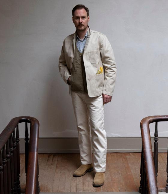 A man wearing a natural canvas Best Made Company chore jacket with matching trousers and suede boots