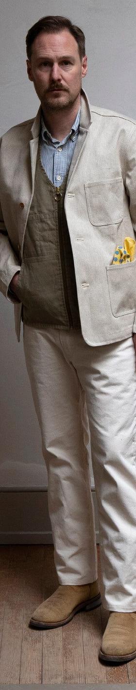 A man wearing a natural canvas Best Made Company chore jacket with matching trousers and suede boots