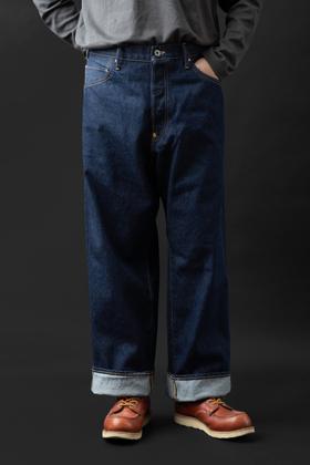 A man wearing wide-leg indigo BIG JOHN selvedge jeans with cuffed hems and brown leather moc-toe boots