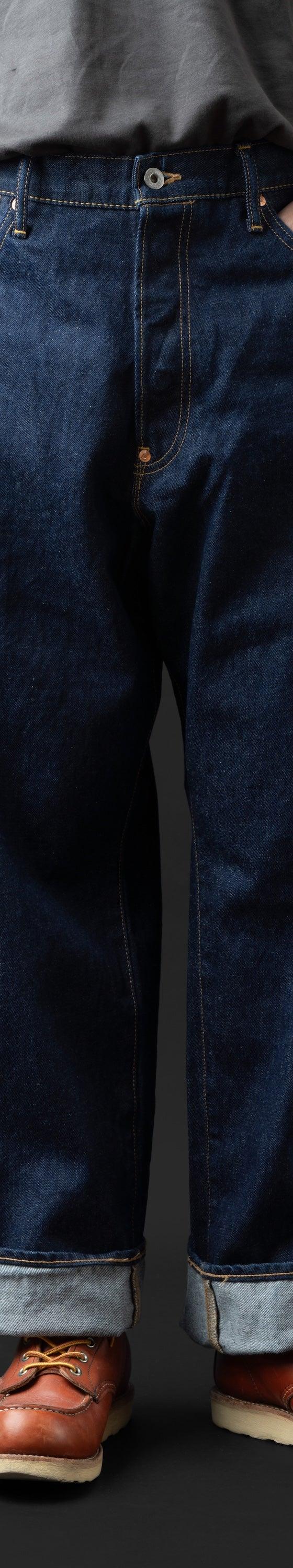 A man wearing wide-leg indigo BIG JOHN selvedge jeans with cuffed hems and brown leather moc-toe boots