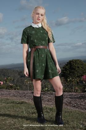 A woman wearing a green printed Black Milk dress with a brown belt and knee-high boots
