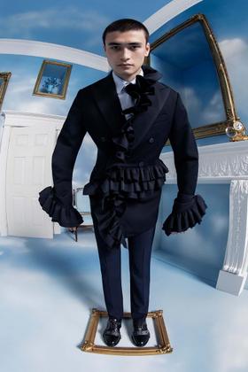 A man wearing a black double-breasted ruffled tailcoat and trousers