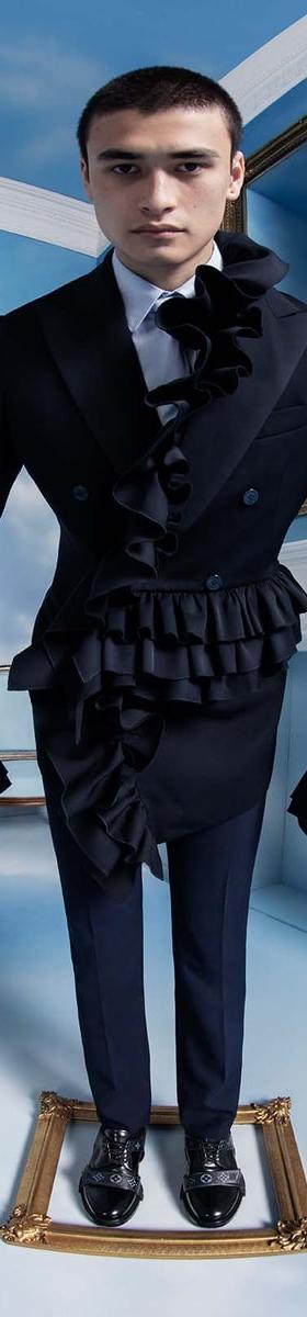A man wearing a black double-breasted ruffled tailcoat and trousers