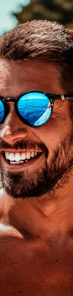 A man wearing blue mirrored Blenders Eyewear polarized sunglasses by the sea