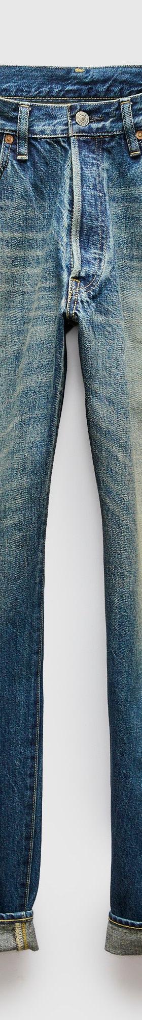 A pair of faded blue selvedge denim jeans with cuffed hems on a plain background