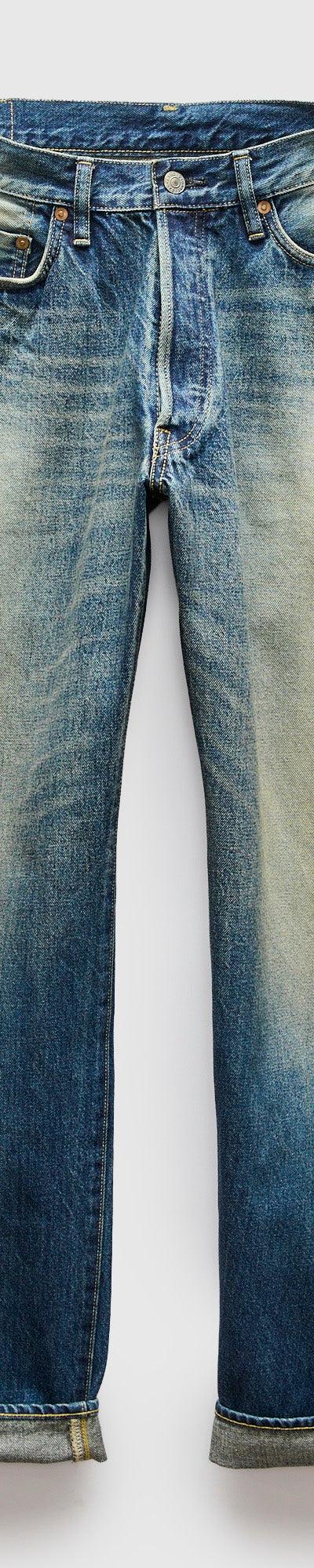 A pair of faded blue selvedge denim jeans with cuffed hems on a plain background