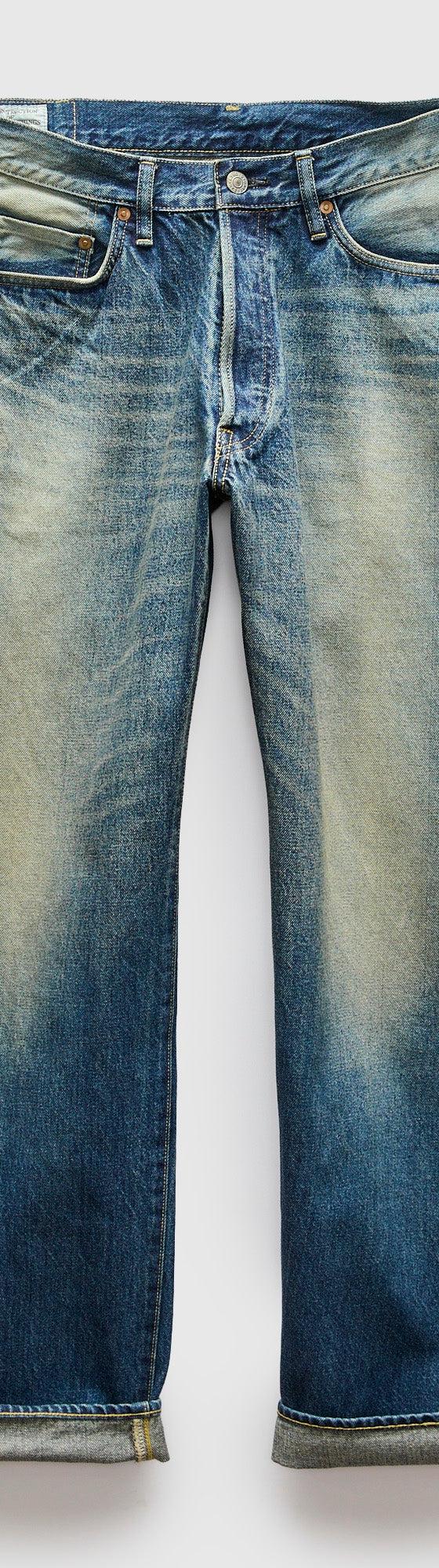 A pair of faded blue selvedge denim jeans with cuffed hems on a plain background