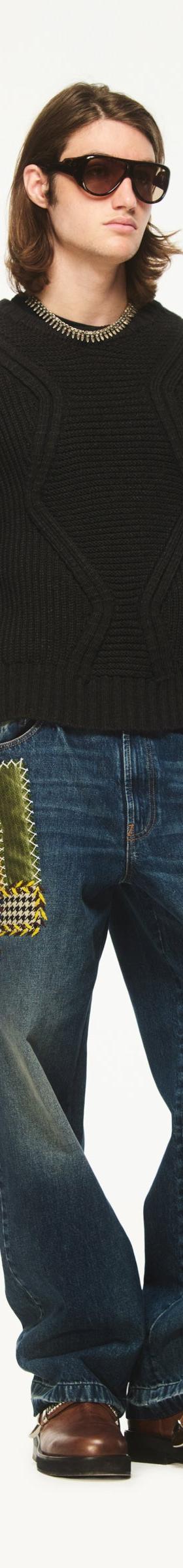 A man wearing a black chunky knit sweater with Bluemarble patchwork-embellished baggy jeans and brown leather shoes
