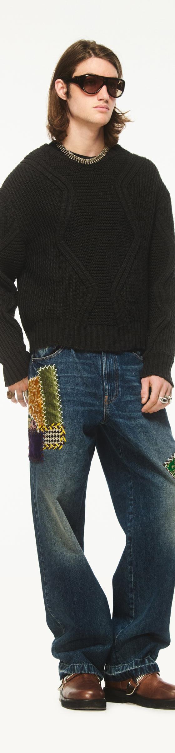 A man wearing a black chunky knit sweater with Bluemarble patchwork-embellished baggy jeans and brown leather shoes
