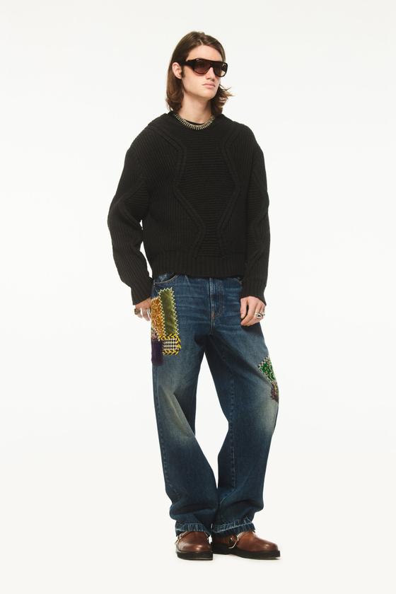 A man wearing a black chunky knit sweater with Bluemarble patchwork-embellished baggy jeans and brown leather shoes
