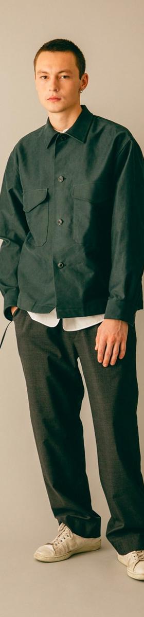 A man wearing a dark green blurhms overshirt with grey wide-leg trousers