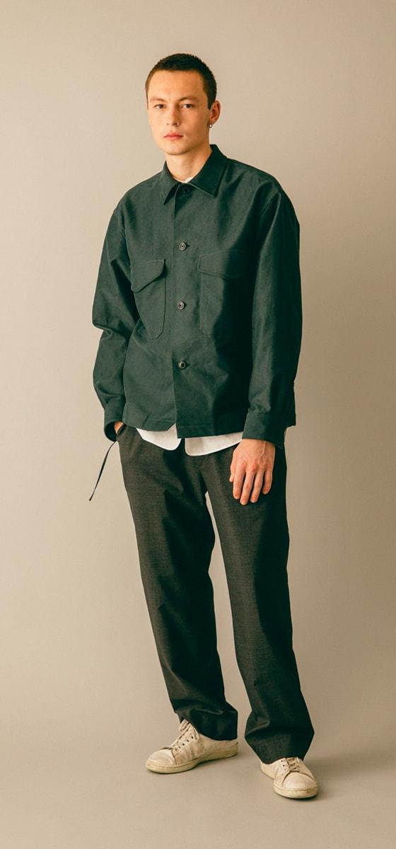 A man wearing a dark green blurhms overshirt with grey wide-leg trousers