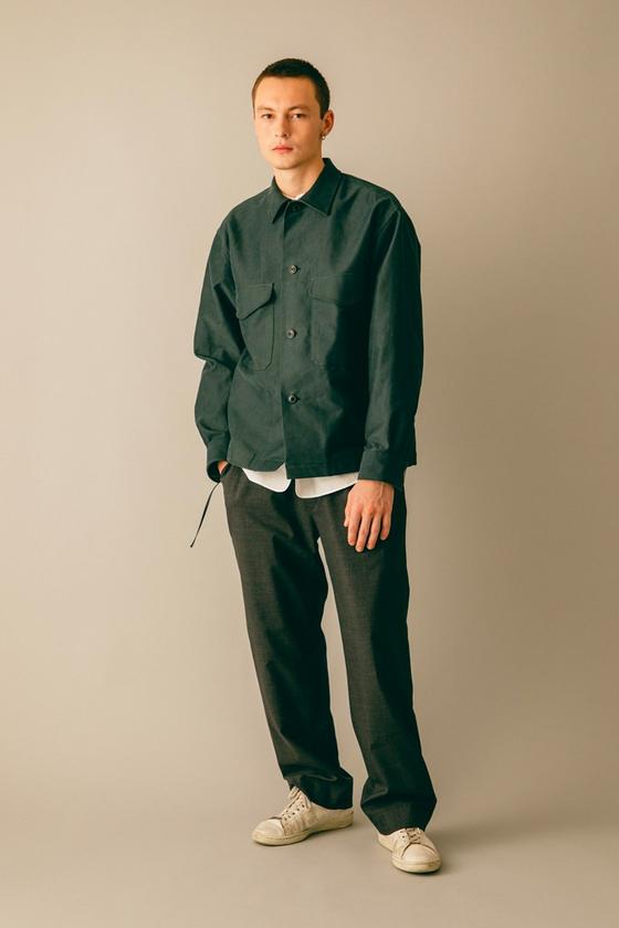 A man wearing a dark green blurhms overshirt with grey wide-leg trousers