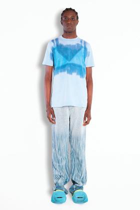A man wearing a blue tie-dye Botter T-shirt with shimmering wave-print trousers and turquoise shell shoes