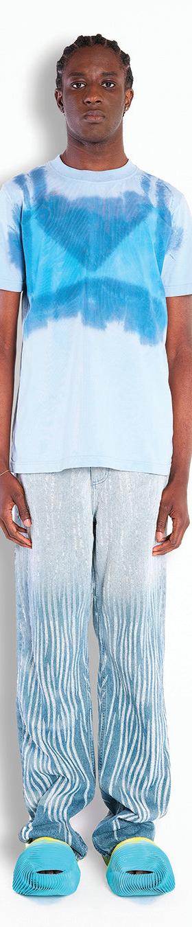 A man wearing a blue tie-dye Botter T-shirt with shimmering wave-print trousers and turquoise shell shoes