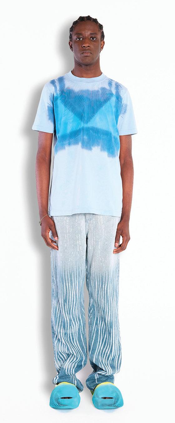 A man wearing a blue tie-dye Botter T-shirt with shimmering wave-print trousers and turquoise shell shoes