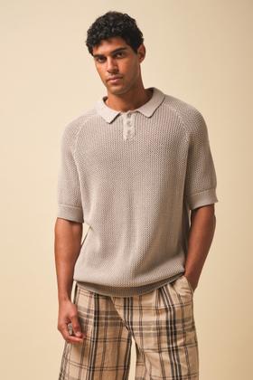 A man wearing a stone open-knit Bound polo shirt with checked trousers