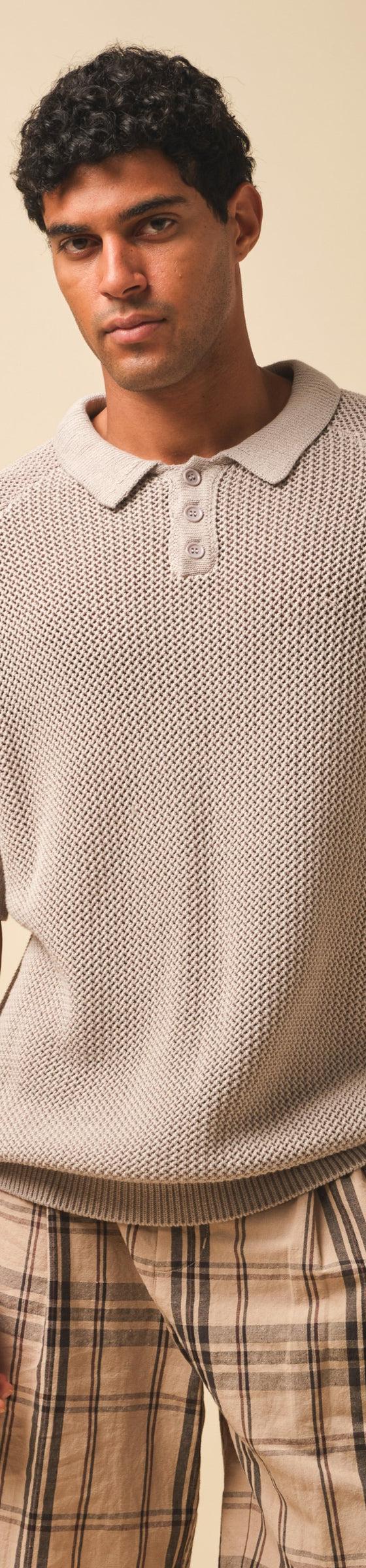 A man wearing a stone open-knit Bound polo shirt with checked trousers
