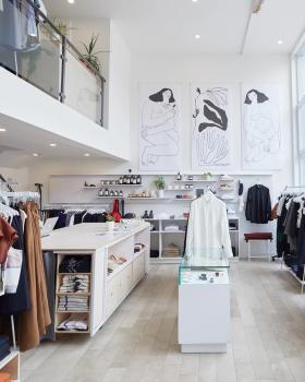The bright interior of a Montreal atelier-boutique with white racks of clothing and line-drawing artwork