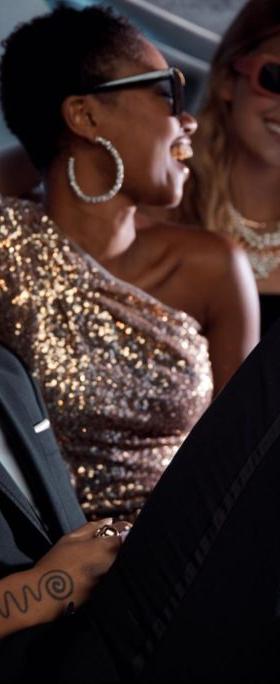A group of people in tailored black and gold eveningwear with sunglasses, seated together in a car interior