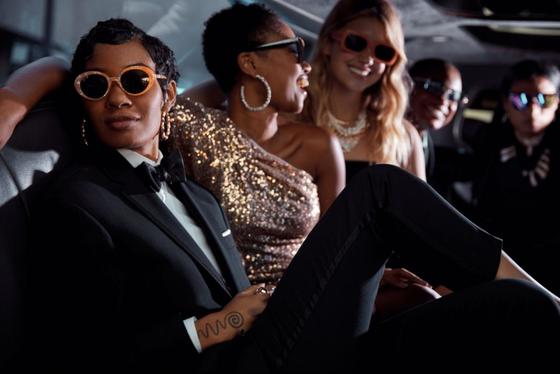 A group of people in tailored black and gold eveningwear with sunglasses, seated together in a car interior