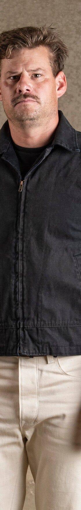 A man wearing a black Bradley Mountain waxed canvas work jacket with cream trousers