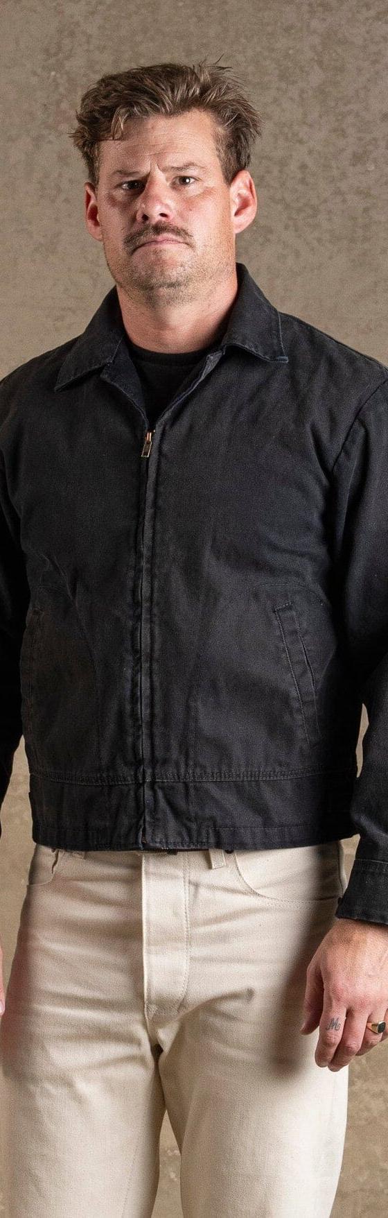 A man wearing a black Bradley Mountain waxed canvas work jacket with cream trousers