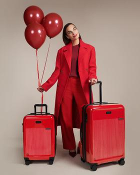 A woman in a red coat standing with two red Briggs & Riley expandable spinner suitcases