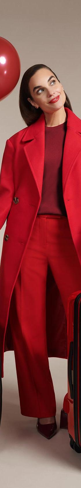 A woman in a red coat standing with two red Briggs & Riley expandable spinner suitcases